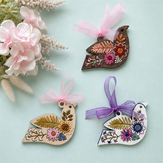 Three folk floral bird embroidery ornaments in light, white and dark wood with pink and purple ribbons