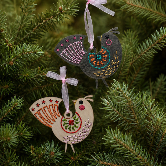 Dark stained and light wood medallion folk bird embroidery ornaments hanging on evergreen branches