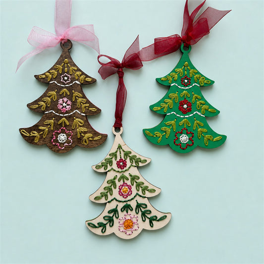 Brown stained, light wood and green tree embroidery ornaments with ribbons on a pale blue background