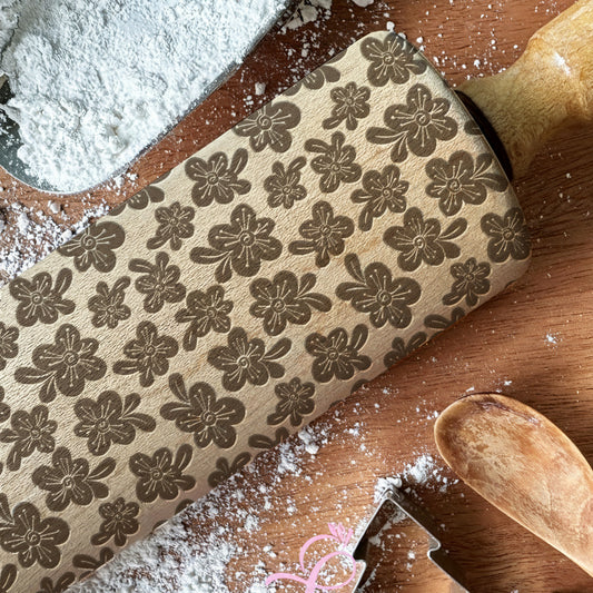 Decorative rolling pin with floral pattern on a wooden surface with cookie cutters and flour.