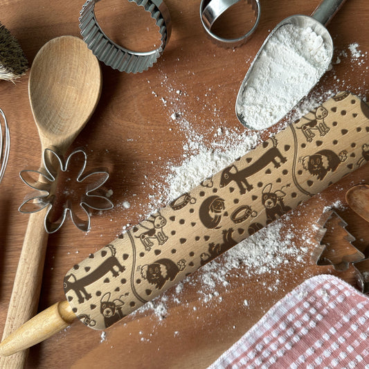 Baking tools including a rolling pin with embossed designs, wooden spoon, and flour sifter on a wooden surface.