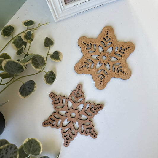Two snowflake trivets on a white surface with green leaves in the background.