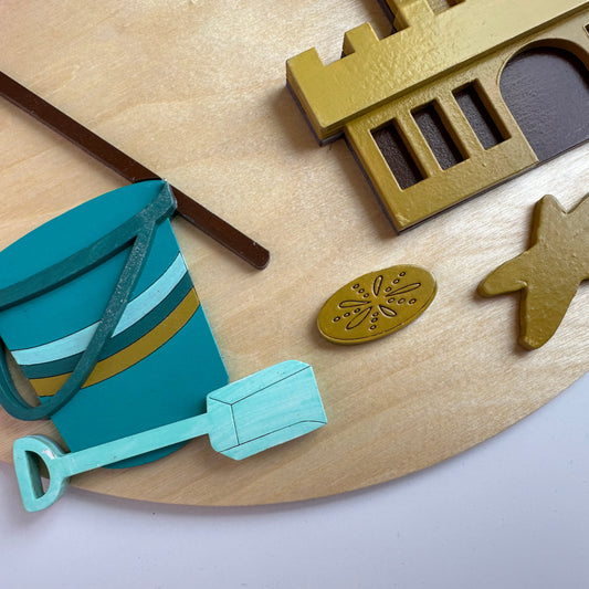 Children's sand toys including a bucket and shovel on a wooden surface with decorative elements.