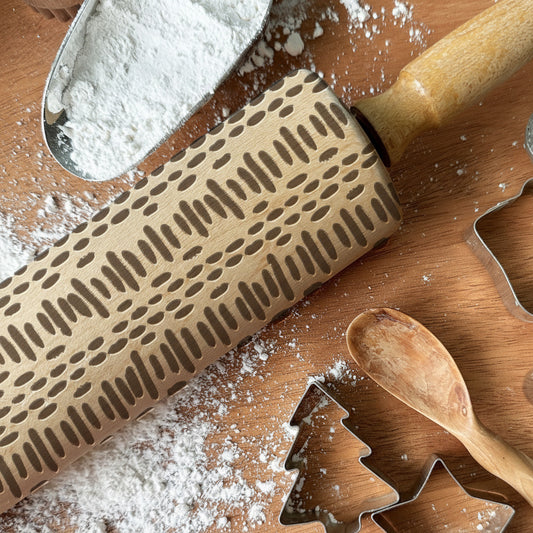 Rolling pin with embossing pattern, cookie cutters, and wooden spoon on a flour-dusted surface with 'Pickle and Peach Studio' branding.