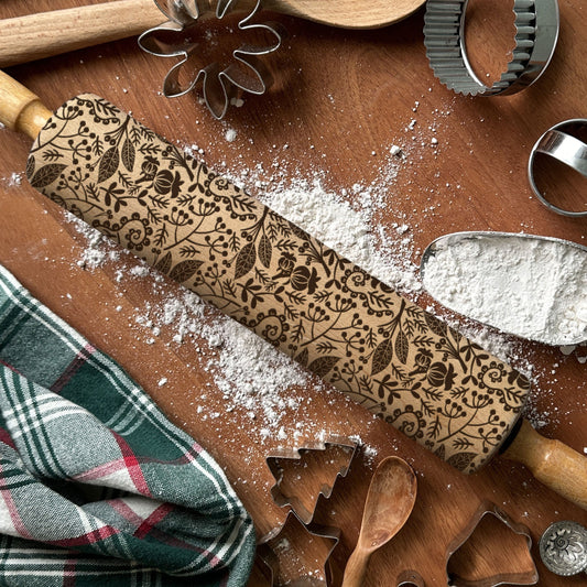 Decorative rolling pin with embossed patterns on a wooden surface with baking tools and flour.