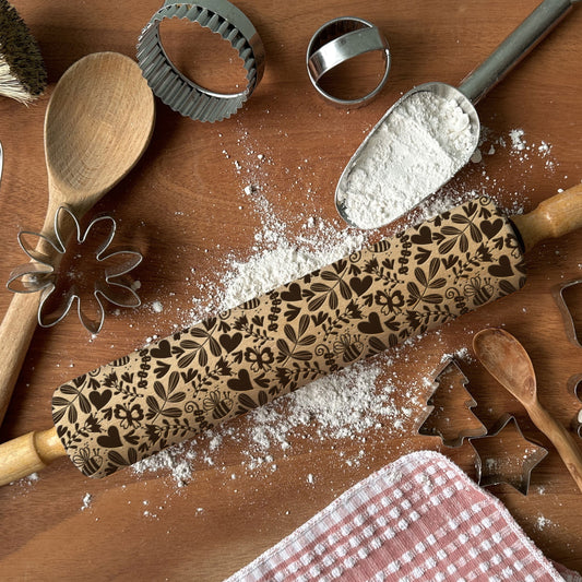 Decorative rolling pin with floral patterns on a wooden surface with flour and baking tools.