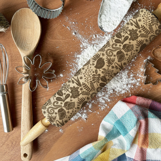 Baking tools and ingredients on a wooden surface with flour, a rolling pin, and cookie cutters.