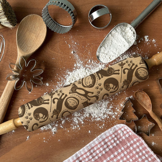 Baking tools including a rolling pin with decorative patterns, wooden spoons, and cookie cutters on a wooden surface.