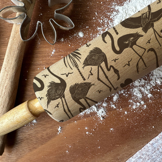 Rolling pin with flamingo pattern on a wooden surface with flour and cookie cutters.