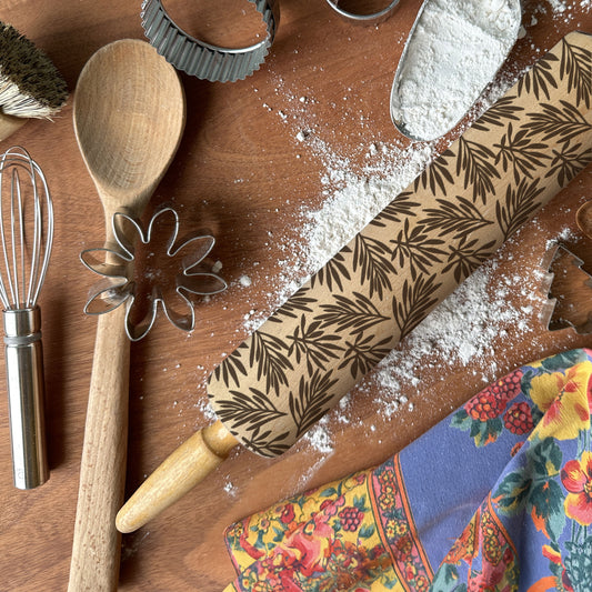 Baking tools including a wooden spoon, rolling pin with leaf pattern, and flour on a wooden surface.