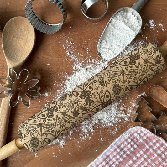 Decorative rolling pin with floral patterns on a wooden surface with baking tools.