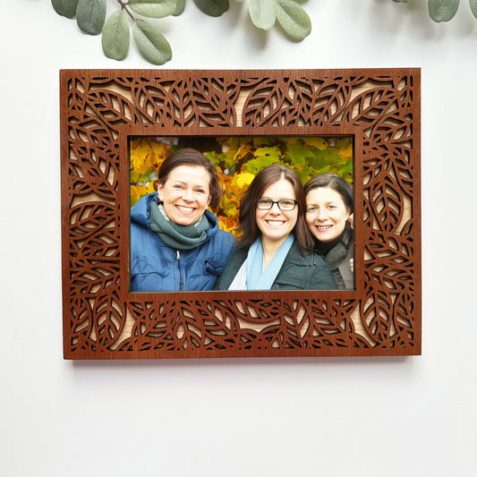 Wooden photo frame with a decorative cut-out design, containing a photo of three people outdoors.