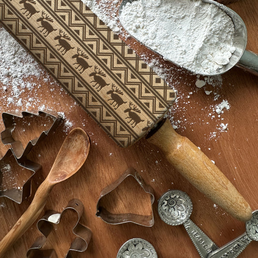 Baking tools including a rolling pin, cookie cutters, and flour on a wooden surface.