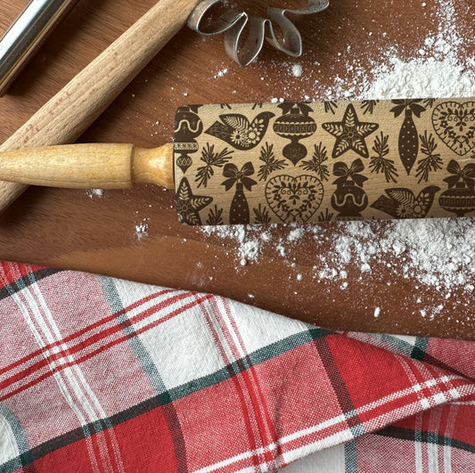 Decorative rolling pin with Christmas patterns on a wooden surface with flour and a plaid cloth.