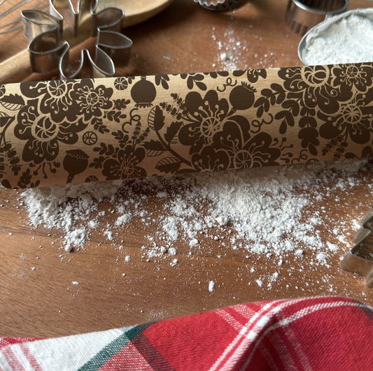 Decorative rolling pin with floral pattern on a wooden surface with flour and cookie cutters.