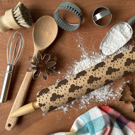 Baking tools including a rolling pin with cookie cutter designs on a wooden surface.