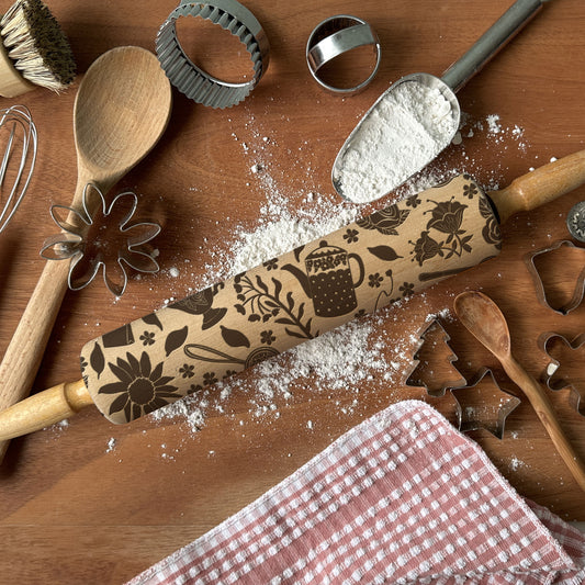 Baking tools including a rolling pin with embossed designs on a wooden surface.