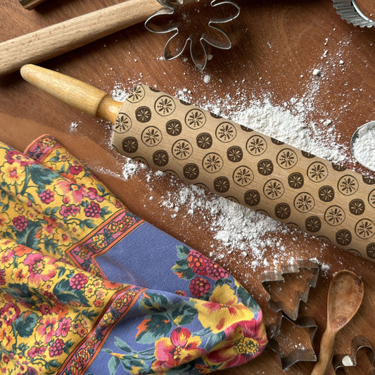 Decorative rolling pin with embossed patterns on a wooden surface with flour and a colorful cloth.