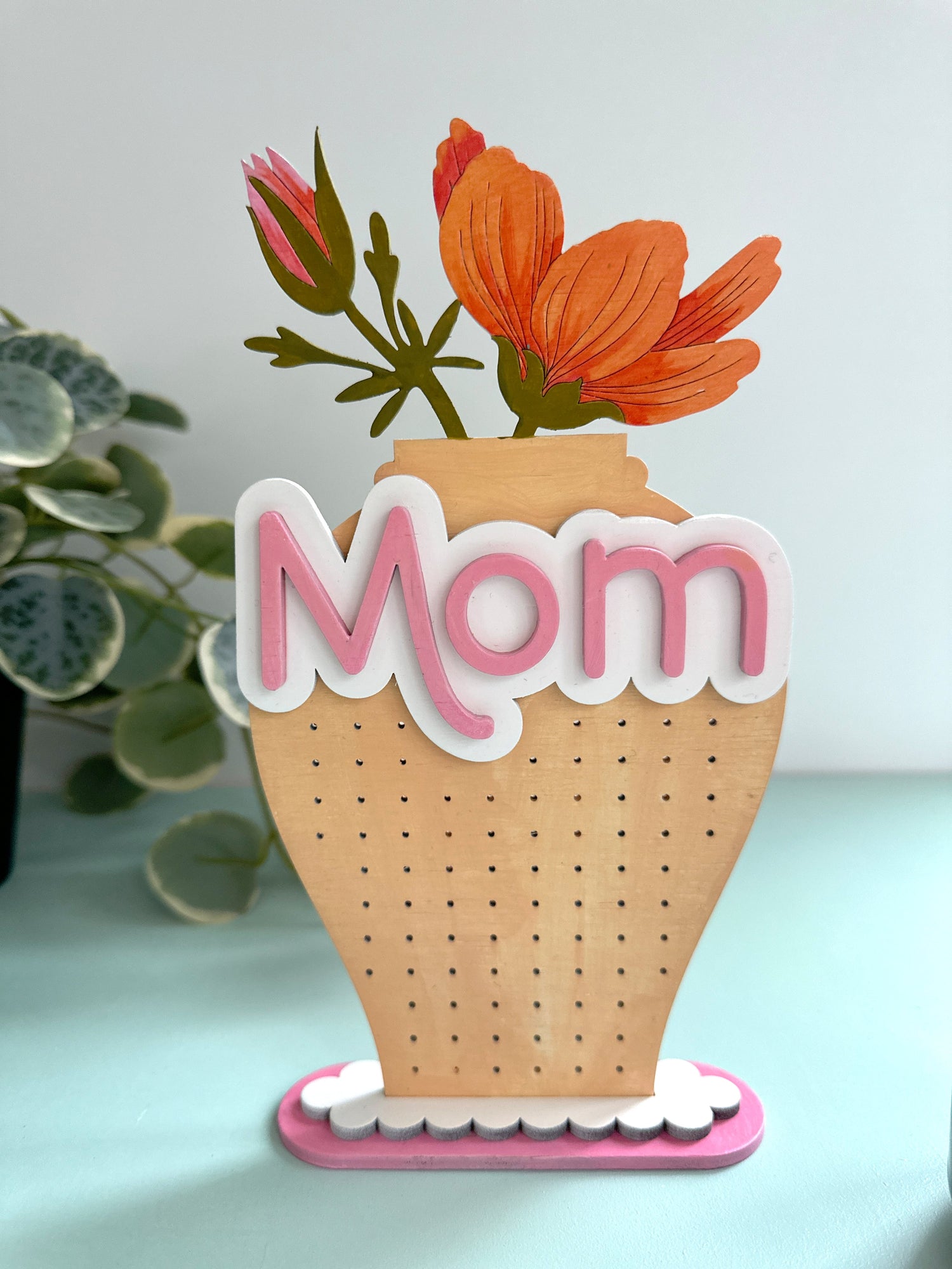 Laser cut earring stand in the shape of a vase with a flower and the word Mom on it.