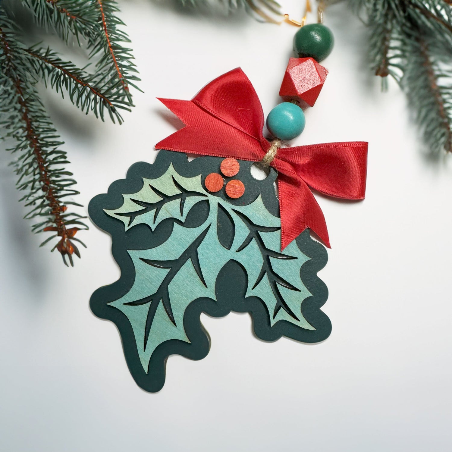 A laser cut holly ornament in spruce green with a red bow.