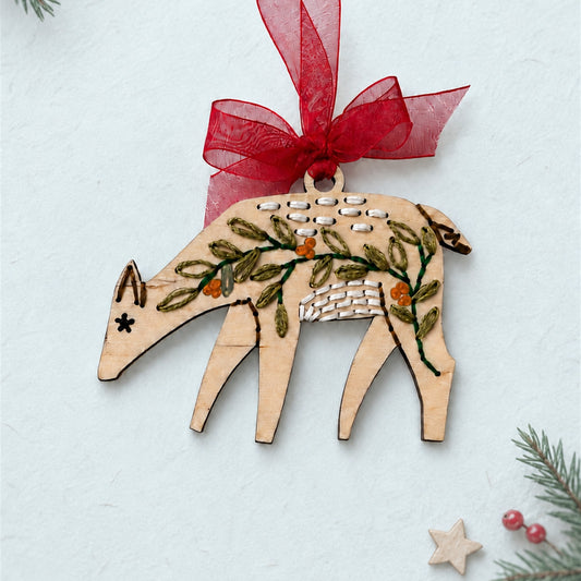 Folk art deer embroidery ornament, light wood deer with green leaf and red berry stitching and a red ribbon