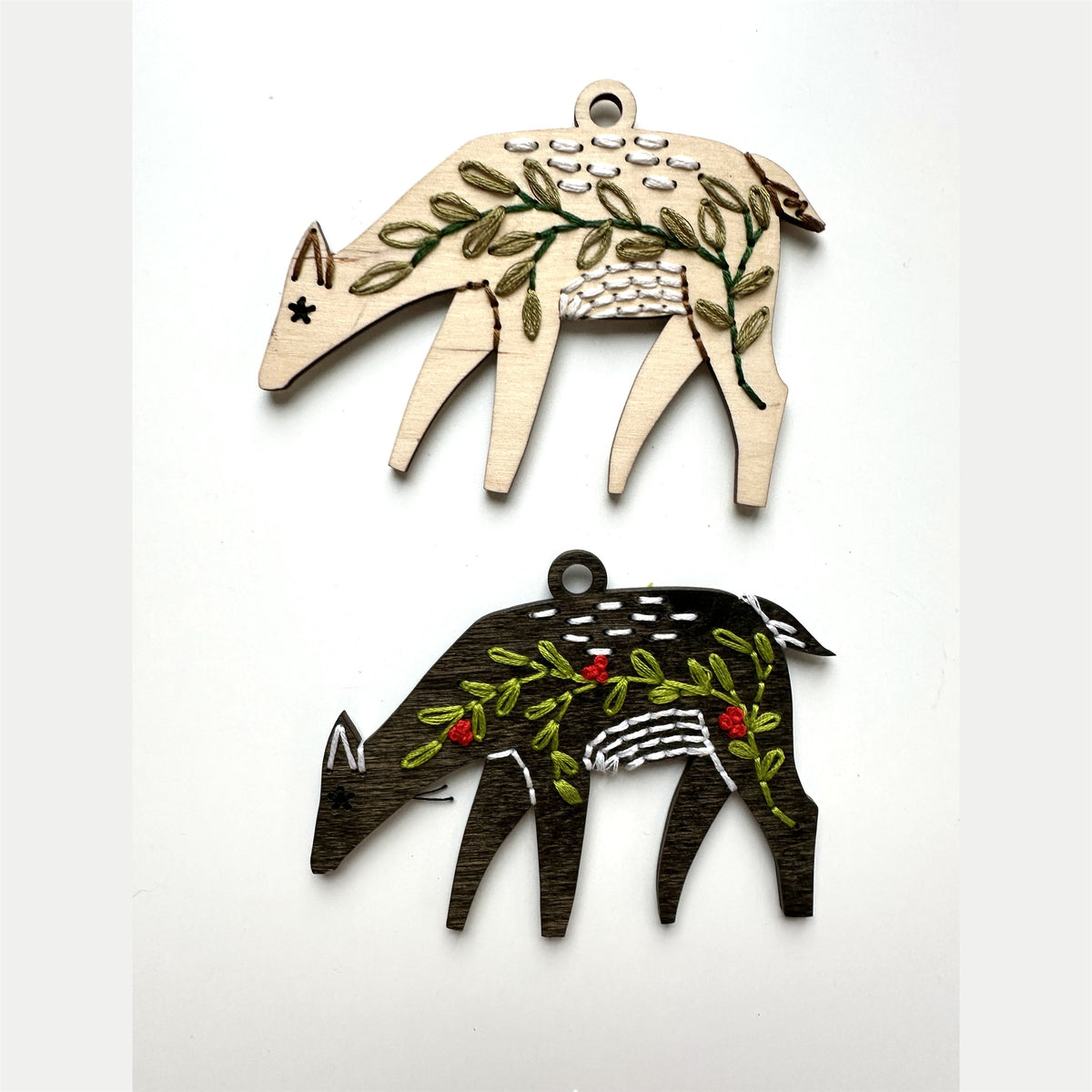 Light wood and dark stained deer embroidery ornaments laid flat on a white background