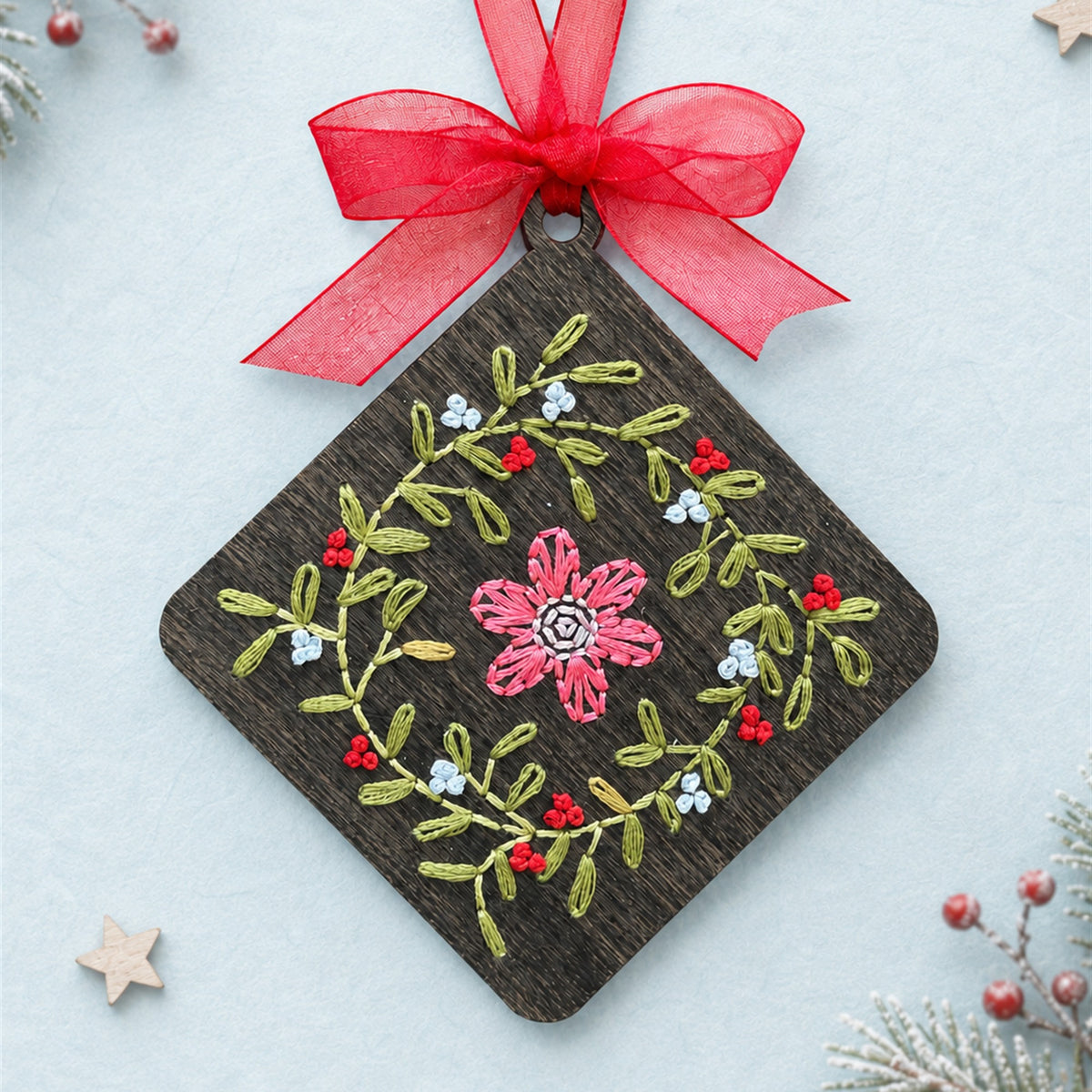 Floral wreath embroidery ornament, dark stained wood diamond with a pink flower and green vine wreath and a red ribbon