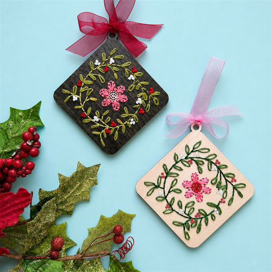Dark stained and light wood floral wreath embroidery ornaments with holly on a pale blue background