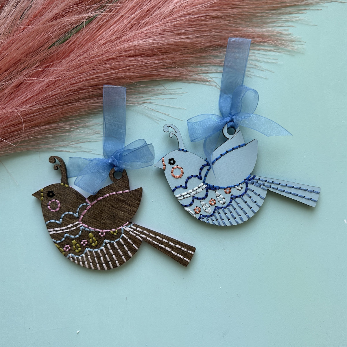 Brown stained and pale blue songbird embroidery ornaments with blue ribbons and pink pampas grass