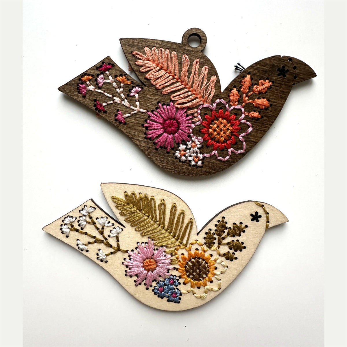 Dark stained and light wood folk floral bird embroidery ornaments laid flat on a white background