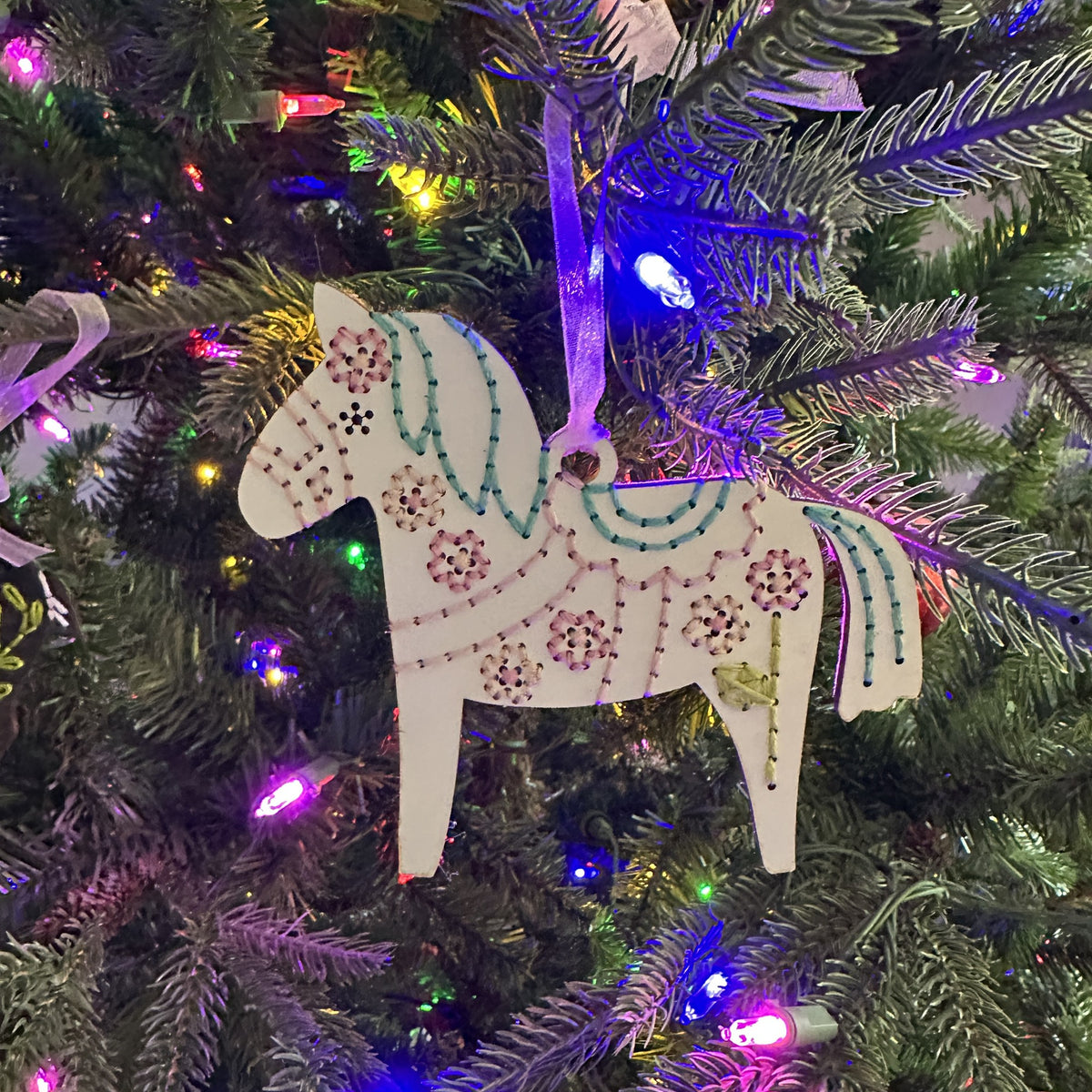 Light wood Dala horse embroidery ornament hanging on a lit Christmas tree
