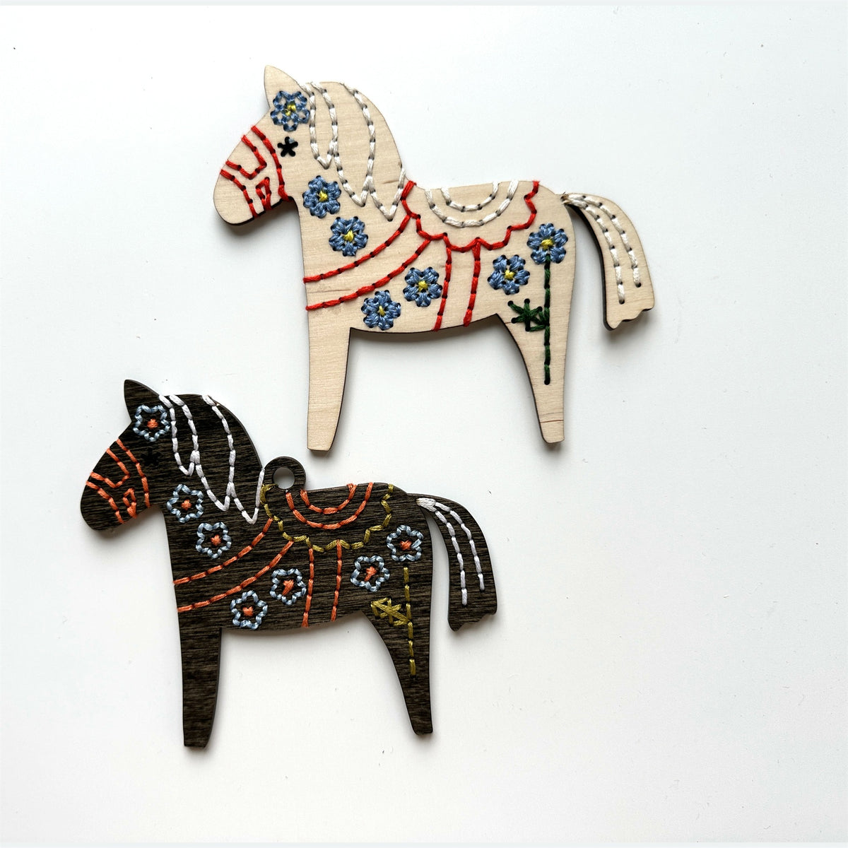 Light wood and dark stained Dala horse embroidery ornaments laid flat on a white background