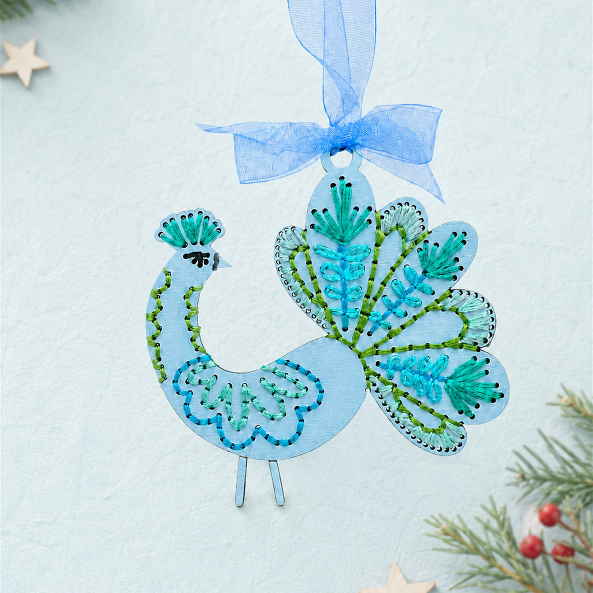 Folk art peacock embroidery ornament, pale blue wood peacock with teal and green stitching and a blue ribbon