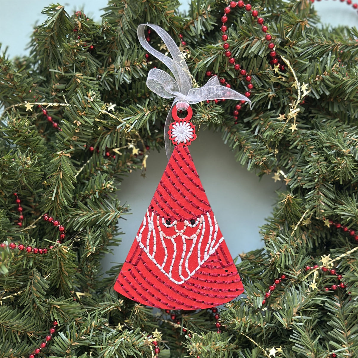 Red Santa embroidery ornament with a white ribbon hanging in an evergreen wreath