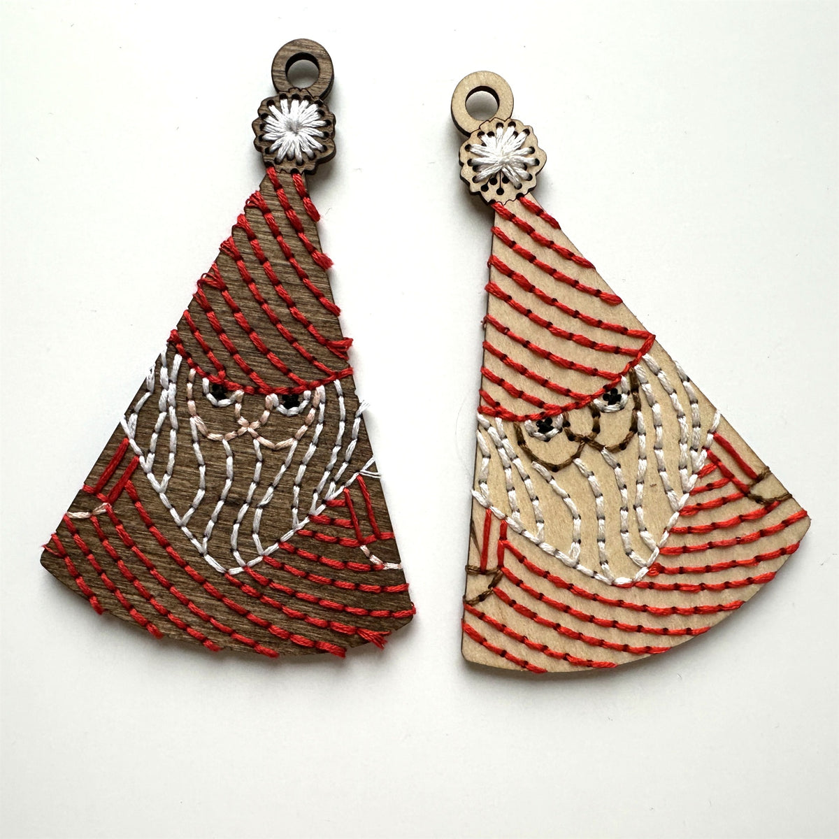 Dark stained and light wood Santa embroidery ornaments laid flat on a white background