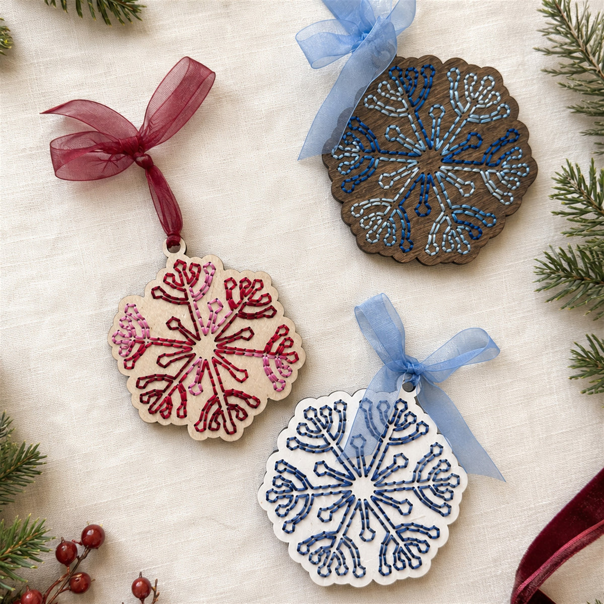 Red, blue and dark stained snowflake embroidery ornaments with ribbons on a white background