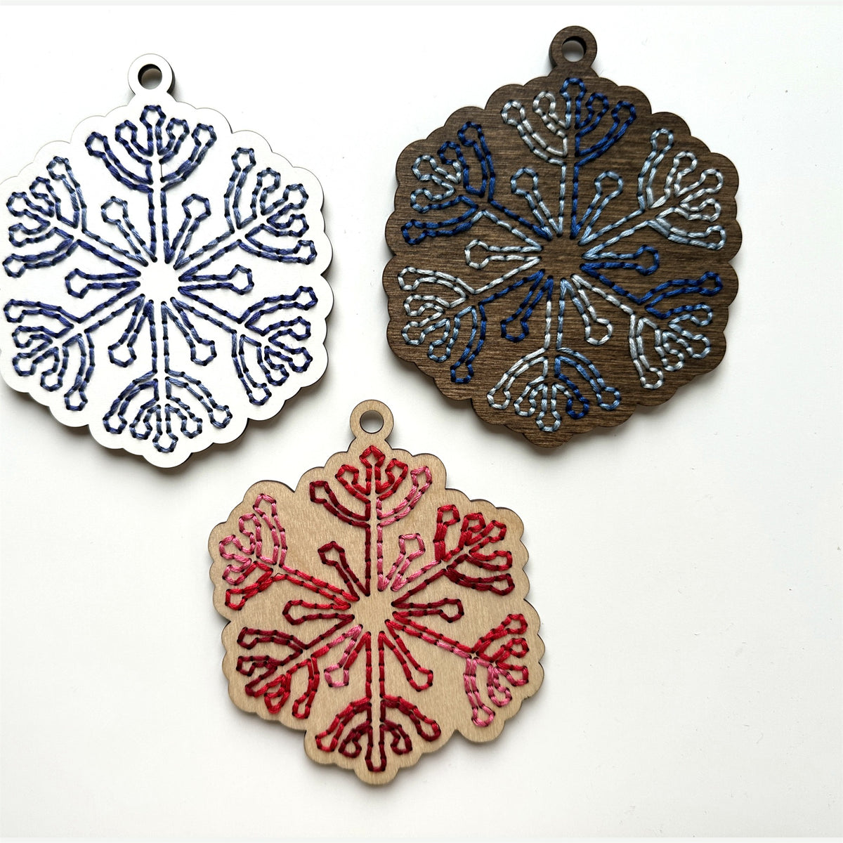 Blue, dark stained and red snowflake embroidery ornaments laid flat on a white background