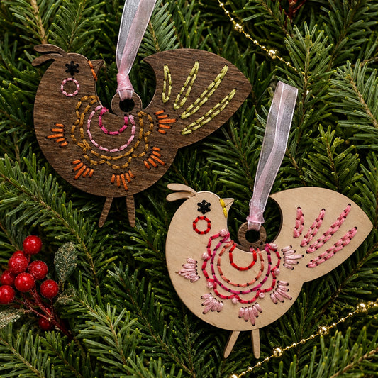 Brown stained and light wood scalloped folk bird embroidery ornaments hanging on evergreen branches
