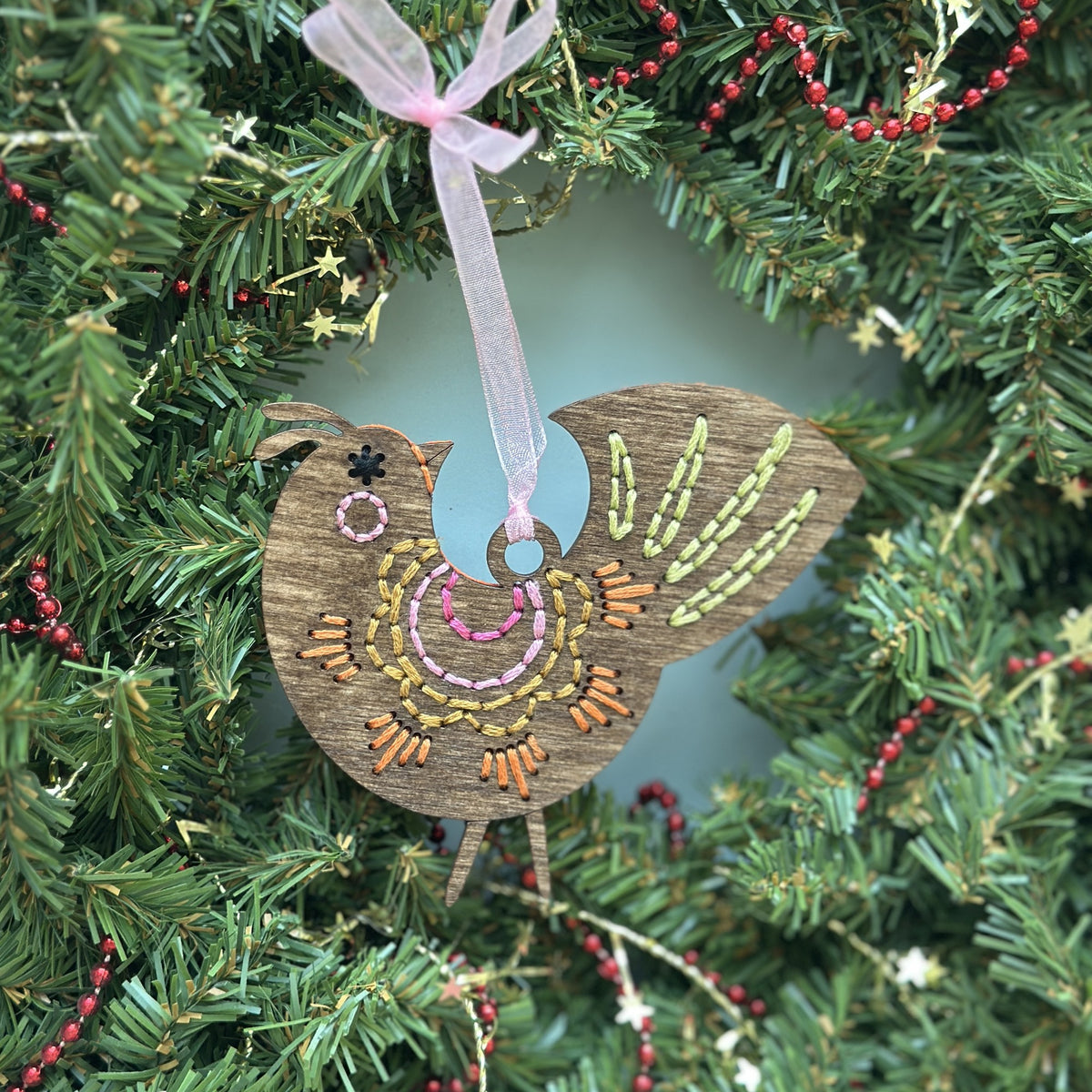 Brown stained scalloped folk bird embroidery ornament hanging in an evergreen wreath