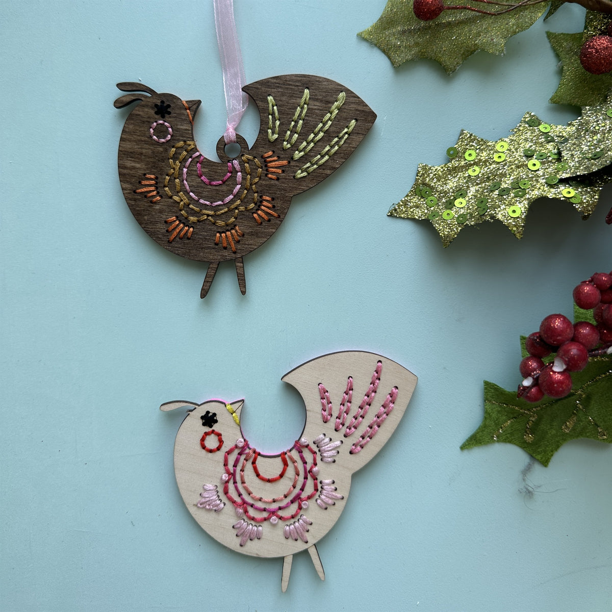 Brown stained and light wood scalloped folk bird embroidery ornaments with holly on a pale blue background