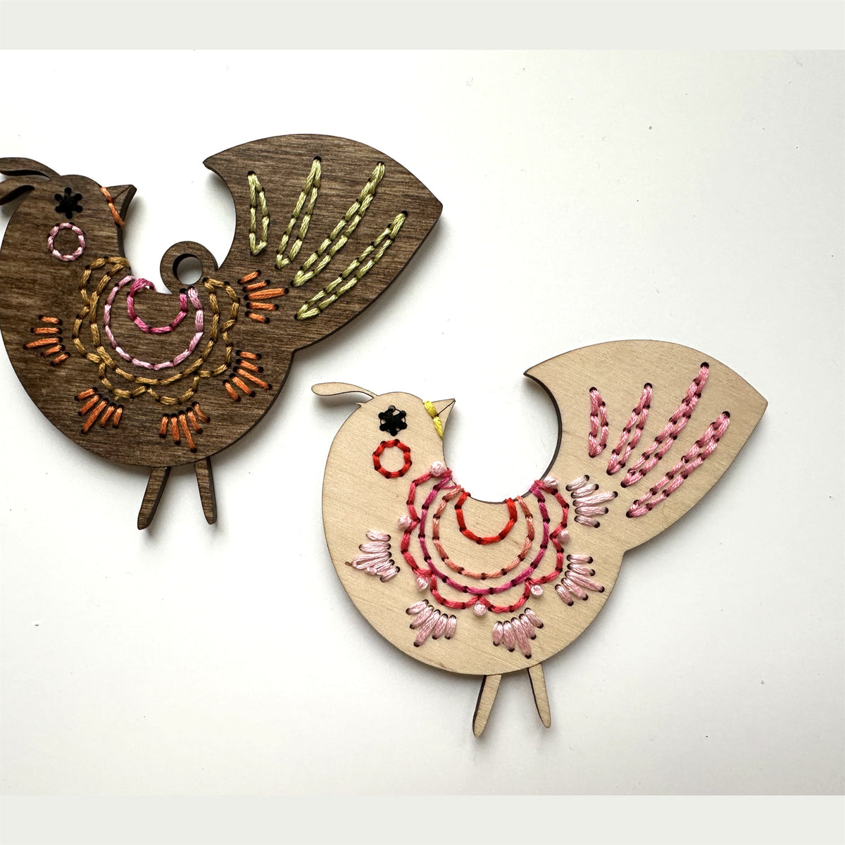 Brown stained and light wood scalloped folk bird embroidery ornaments laid flat on a white background