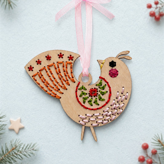 Medallion folk bird embroidery ornament, light wood bird with red stars, orange feather stitching and a pink ribbon