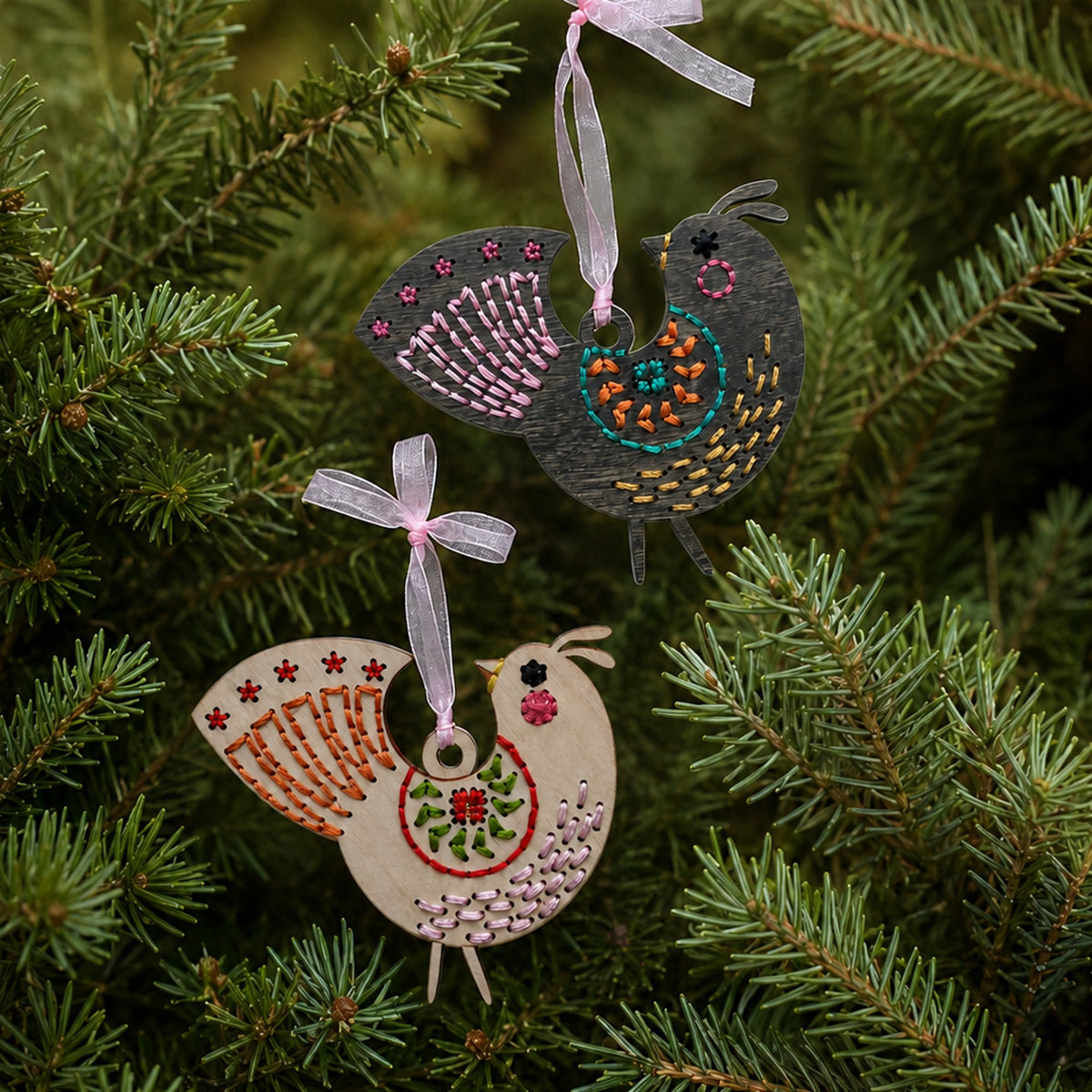 Dark stained and light wood medallion folk bird embroidery ornaments hanging on evergreen branches