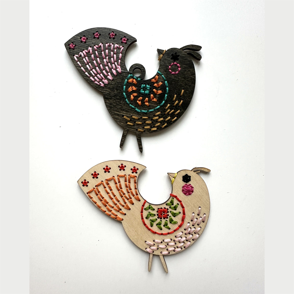Dark stained and light wood medallion folk bird embroidery ornaments laid flat on a white background