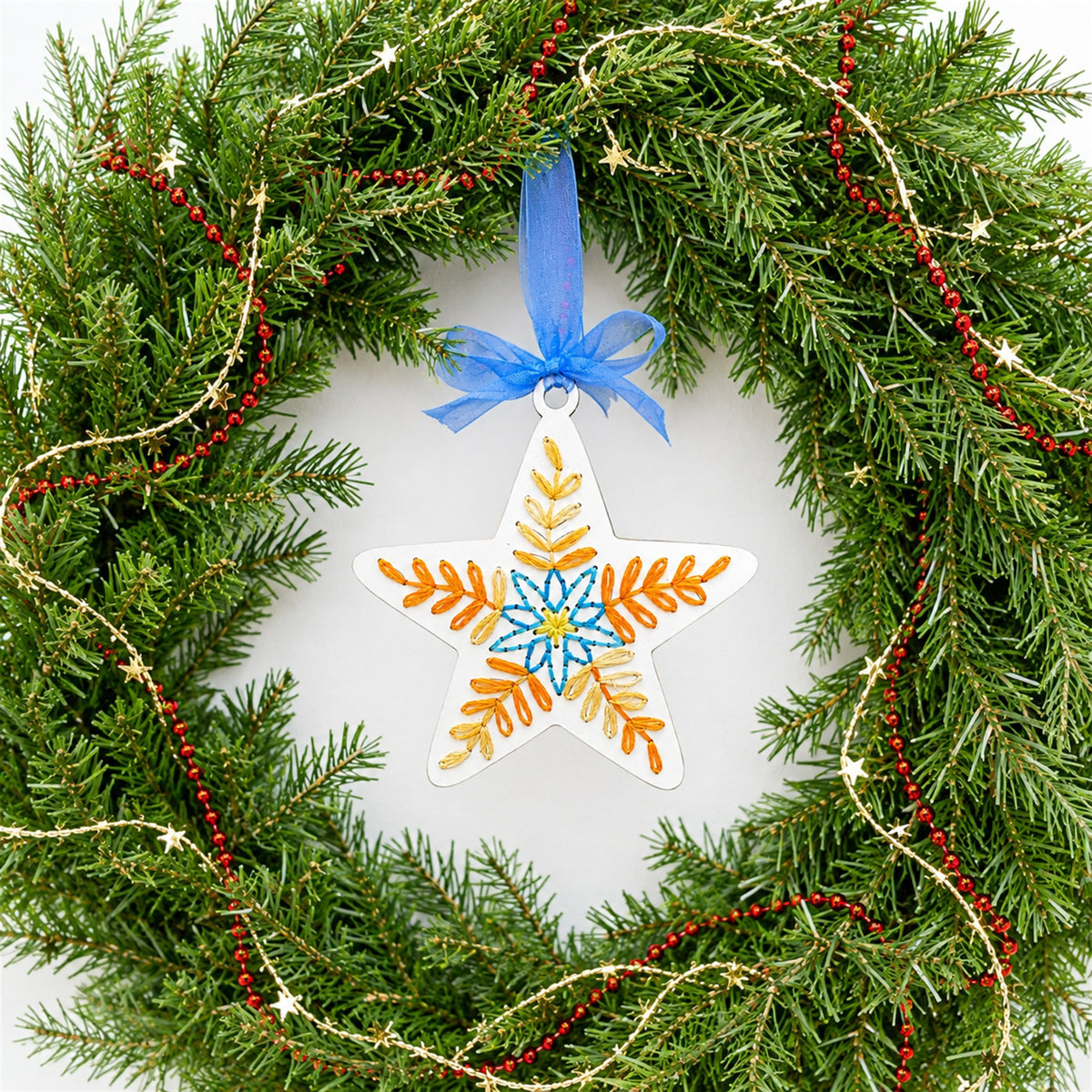 Folk art star embroidery ornament hanging in an evergreen Christmas wreath
