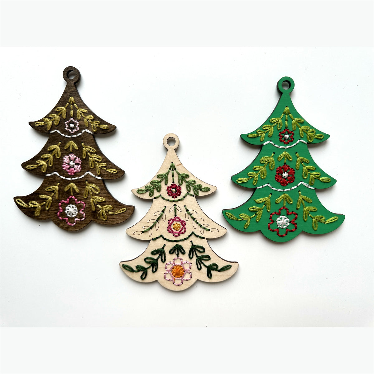 Brown stained, light wood and green tree embroidery ornaments laid flat on a white background
