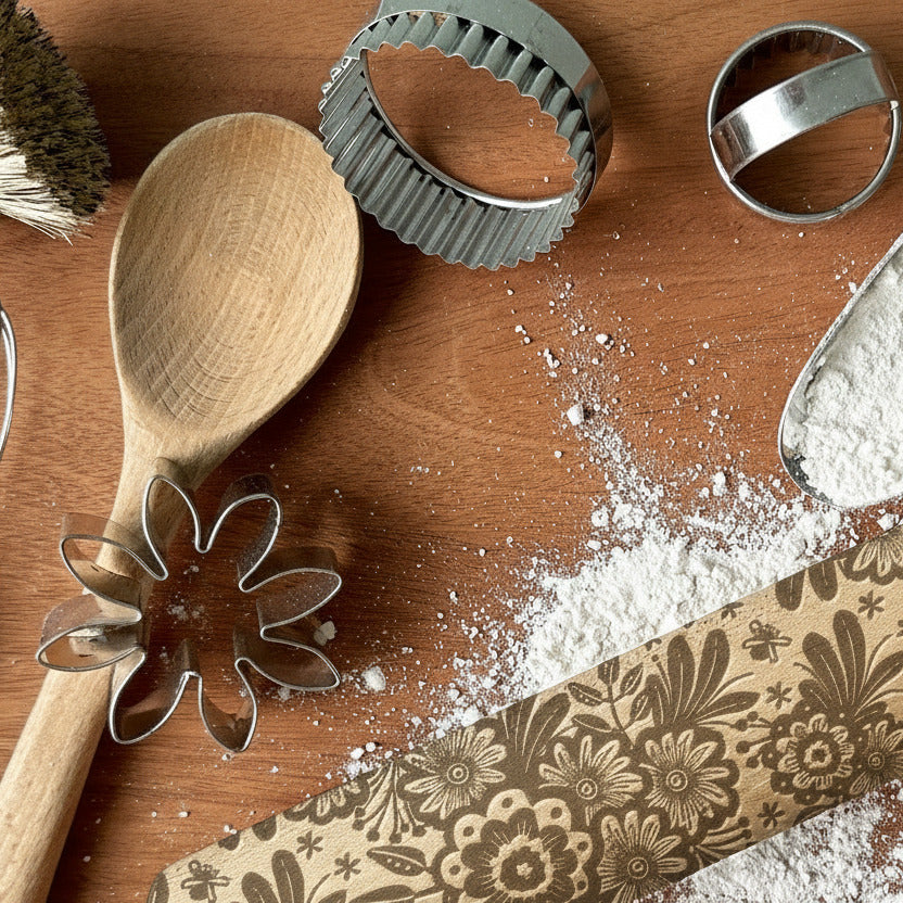 Wooden rolling pin with floral patterns on a wooden surface with baking tools.