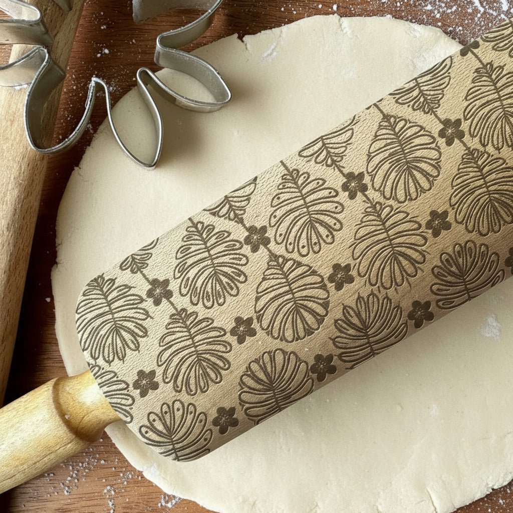 Rolling pin with leaf pattern on a wooden surface with flour, cookie cutters, and 'PickleandPeachStudio' branding.