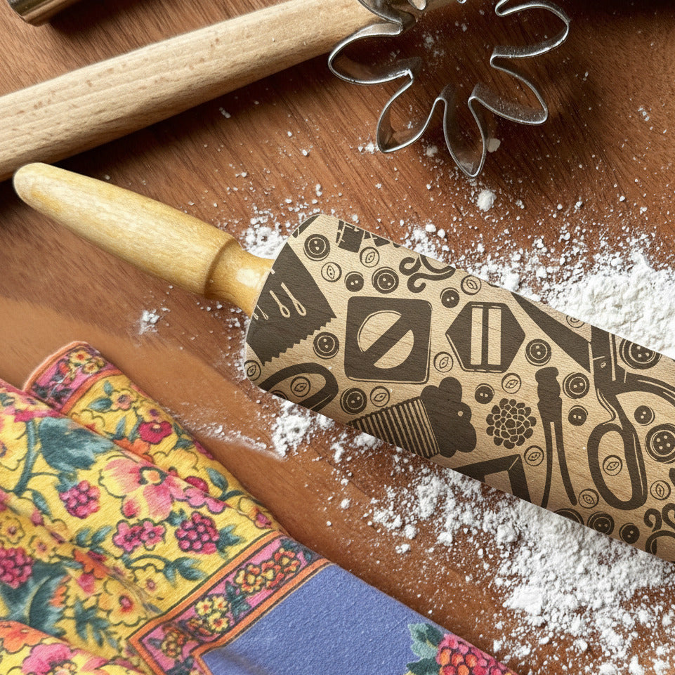 Decorative rolling pin with pattern on a wooden surface with flour, surrounded by cookie cutters and a colorful fabric.