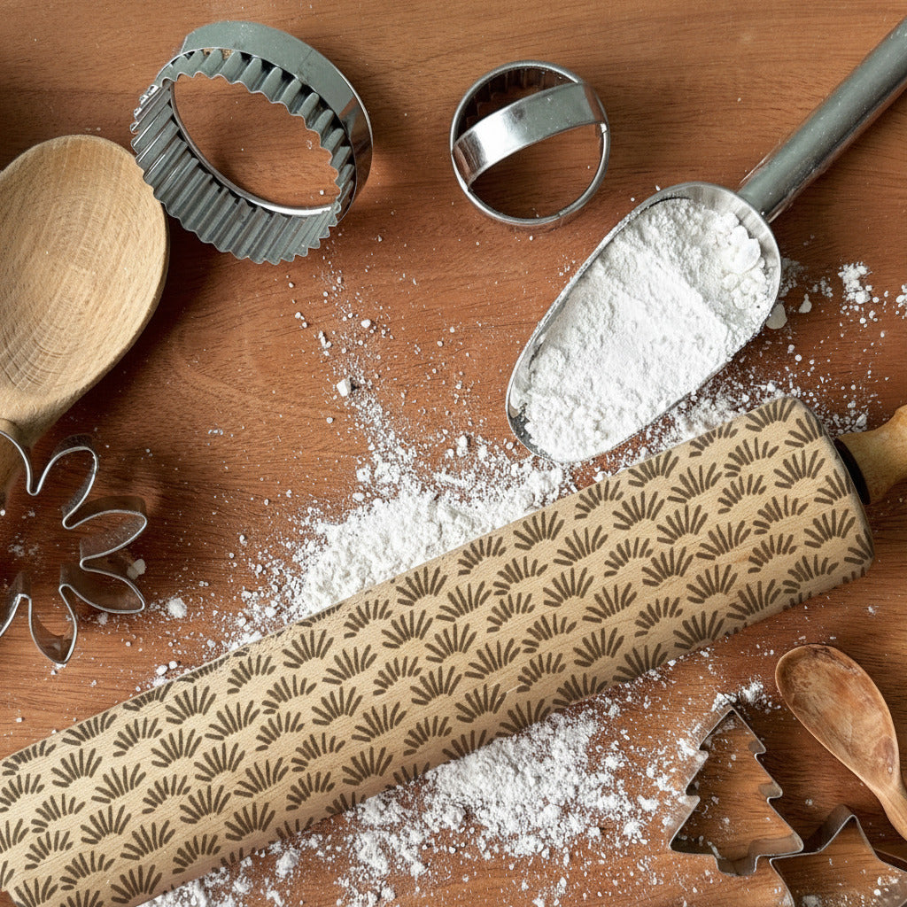 Baking tools including a rolling pin, wooden spoon, and cookie cutters on a wooden surface with flour.